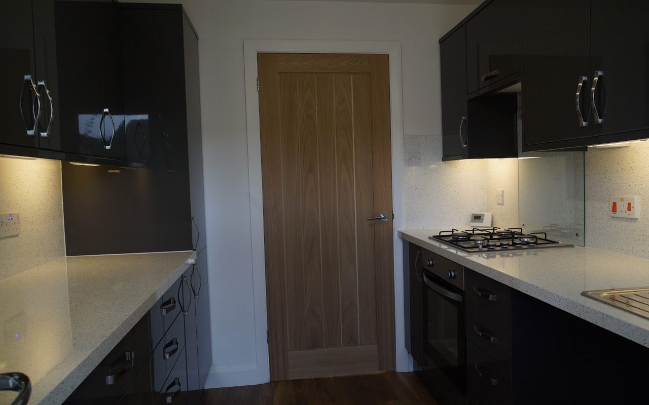 The same kitchen finished: gloss charcoal units, sparkle quartz worktops, a gas hob and an oak door