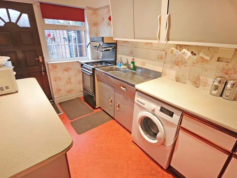 The kitchen before: cream wall units, floral tiles, a freestanding cooker and a red tiled floor