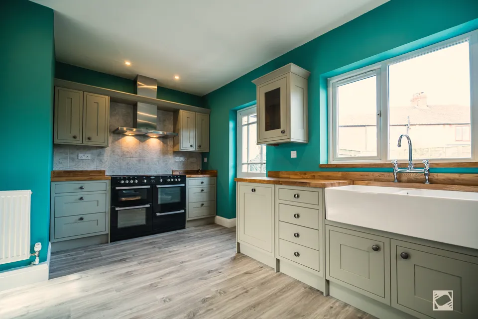 Sage green shaker kitchen with oak worktops, a Belfast sink under the window and a black range cooker