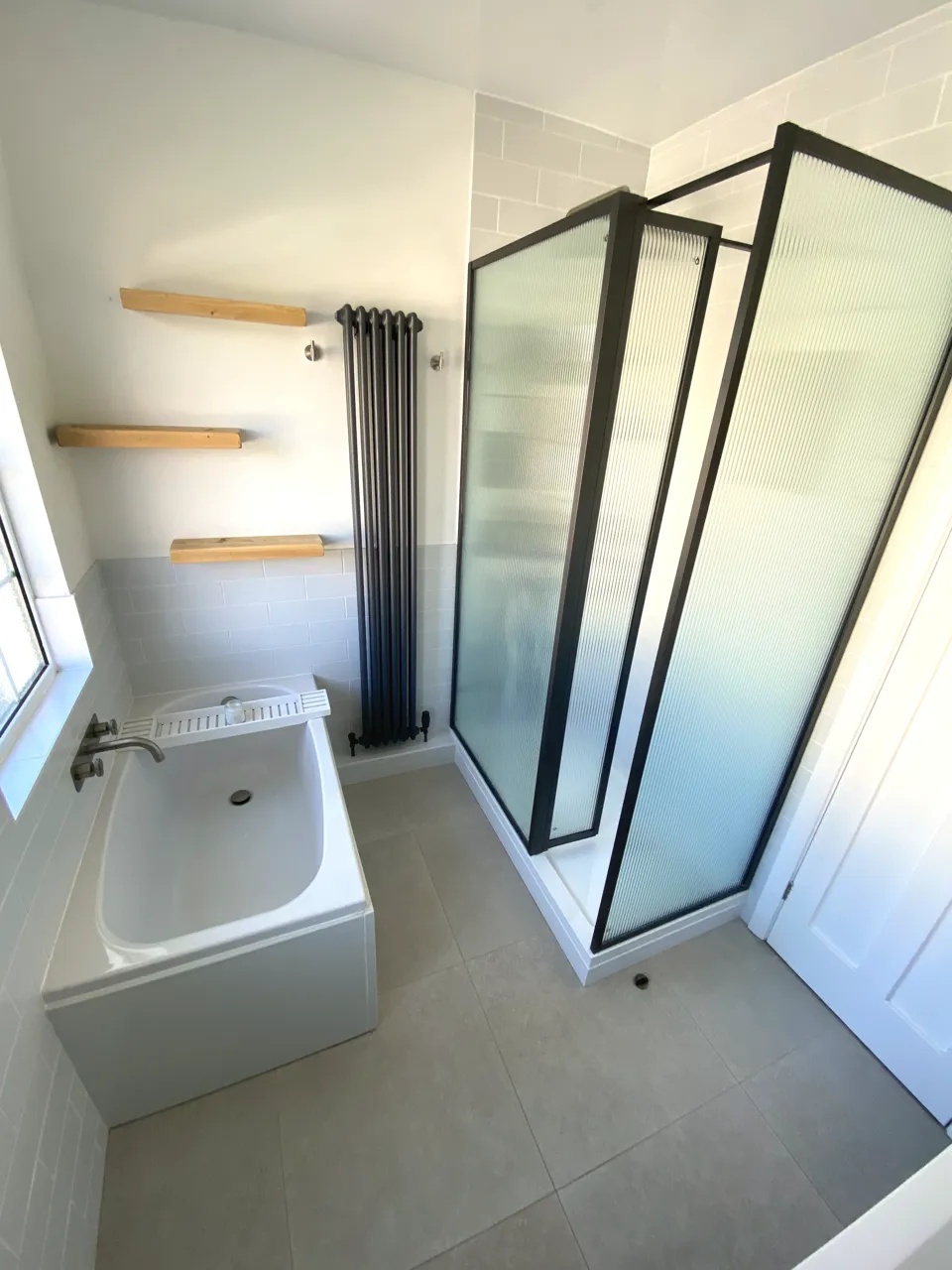 Bathroom with a black-framed reeded glass shower enclosure, a bath, a black column radiator and oak shelves