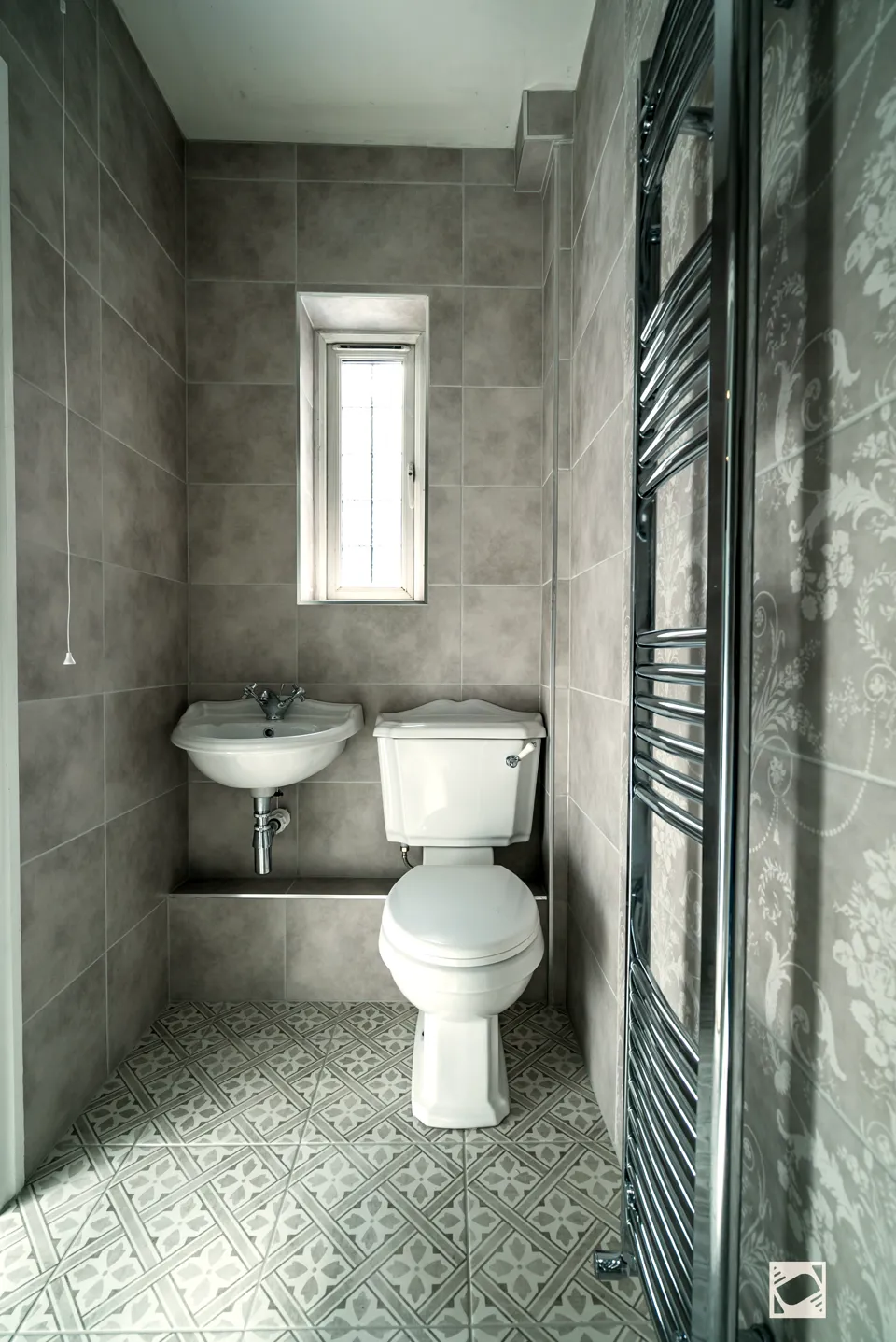 Shower room with grey tiles, a traditional WC and wall basin, a tall chrome towel rail and patterned floor tiles