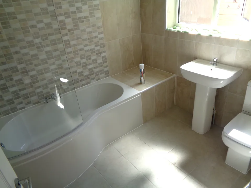 Cream bathroom with a P-shaped shower bath, a mosaic feature wall and a pedestal basin
