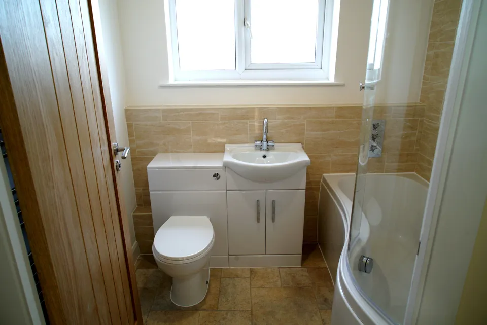 Bathroom with a white gloss vanity and WC combination unit, a shower bath with a curved screen and an oak door