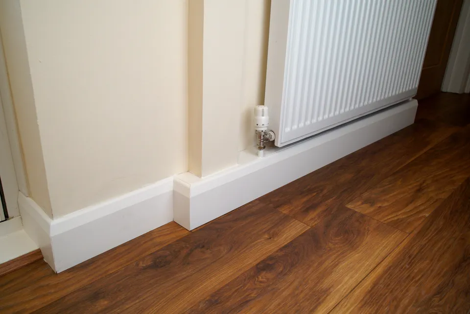 Walnut-effect laminate floor finished with new white skirting beside a radiator