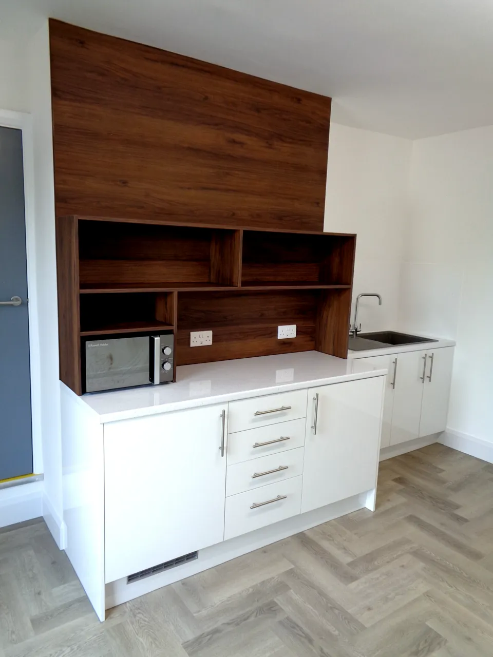 White gloss kitchen units under a full-height walnut panel with open shelving and a microwave