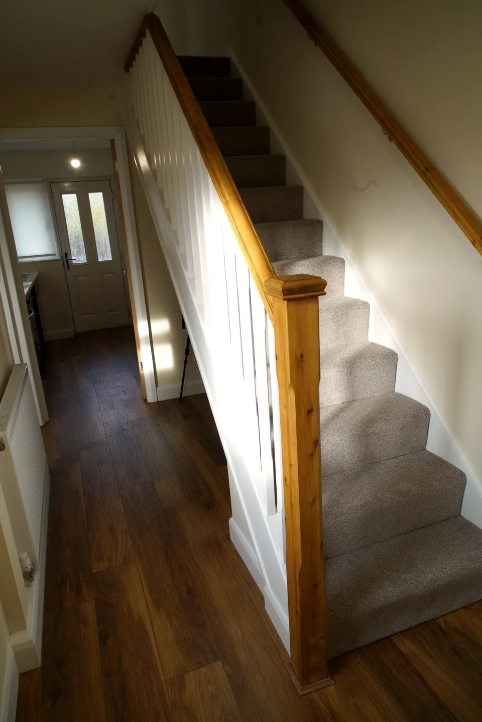 Staircase with white spindles, a pine handrail and newel post, grey carpet and a dark wood-effect hall floor
