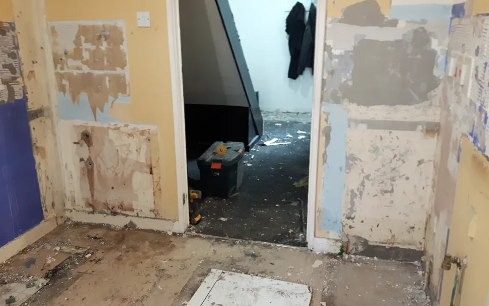 Before: the kitchen stripped back to bare walls and floor, looking through the doorway to the hall